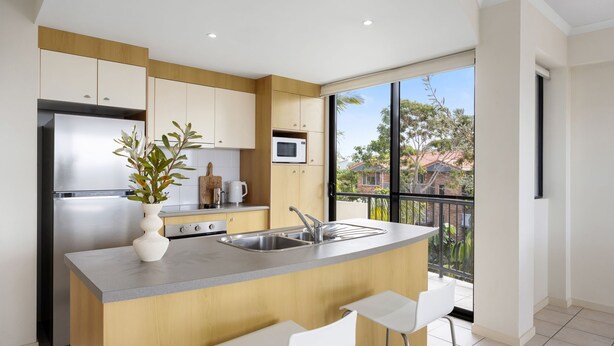 A modern kitchen with a central island, stainless steel appliances, and a view of the neighborhood. - First Avenue Glade 6 (Coolum Beach)