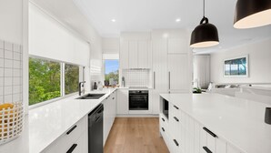 Een moderne keuken met witte kasten, een inbouwoven en een groot raam met uitzicht op groen.
