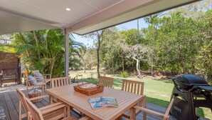 An outdoor patio with a wooden table, chairs, a grill, and a magazine. - Ashton Villa 1 Peregian Beach (Peregian Beach)