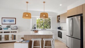 A modern kitchen with a central island, stainless steel appliances, and a large window with a view of palm trees. - Sunbright 1 Peregian Beach (Peregian Beach)