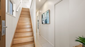 A modern interior with a wooden staircase leading to a landing, a white wall with a painting, and a potted plant. - Dune Grove 9 Peregian Beach (Peregian Beach)