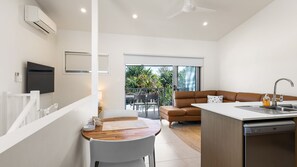 Una cocina moderna con lavavajillas integrado, un comedor con mesa y sillas de madera, un sofá de cuero marrón y un balcón con vistas a zonas verdes.