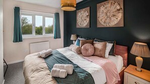 Ein Schlafzimmer mit einem Bett, zwei Wandlampen, einem Fenster mit Vorhängen und zwei Wandbildern.