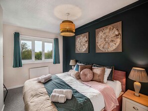 Ein Schlafzimmer mit einem Bett, zwei Wandlampen, einem Fenster mit Vorhängen und zwei Wandbildern.