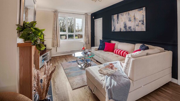 Ein Wohnzimmer mit einem beigen Sofa, einem Couchtisch, einer Kristallleuchter und einem großen abstrakten Gemälde an der Wand.
