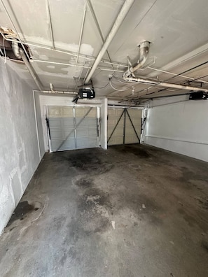 A garage with concrete floor and walls, two garage doors, and visible HVAC ducts and pipes. - Charming 1 Bedroom apt in Beverly Hills (Beverly Hills)