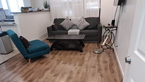 Un saló modern amb una butaca color turquesa, un sofà fosc amb coixinets grisos, una taula de centre i una làmpada de peu.