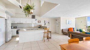 A modern kitchen with white cabinets, a central island, and a hanging plant. - Blue Horizon Peregian (Peregian Beach)