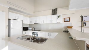 A modern kitchen with white cabinets, stainless steel appliances, and a sink. - Blue Horizon Peregian (Peregian Beach)