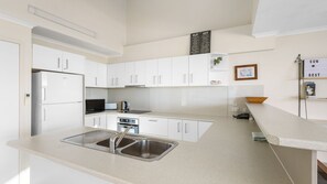 A modern kitchen with white cabinets, stainless steel appliances, and a sink. - Blue Horizon Peregian (Peregian Beach)
