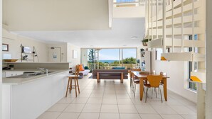 A modern kitchen with a dining area, a balcony with a view, and a living room with a sofa and chairs. - Blue Horizon Peregian (Peregian Beach)