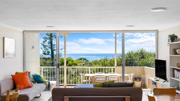 A modern living room with a large sliding glass door leading to a balcony with a view of the ocean. - Blue Horizon Peregian (Peregian Beach)