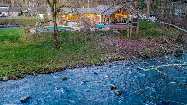 Un chalet au bord de la rivière, doté d’une piscine, entouré d’arbres et d’une pelouse.