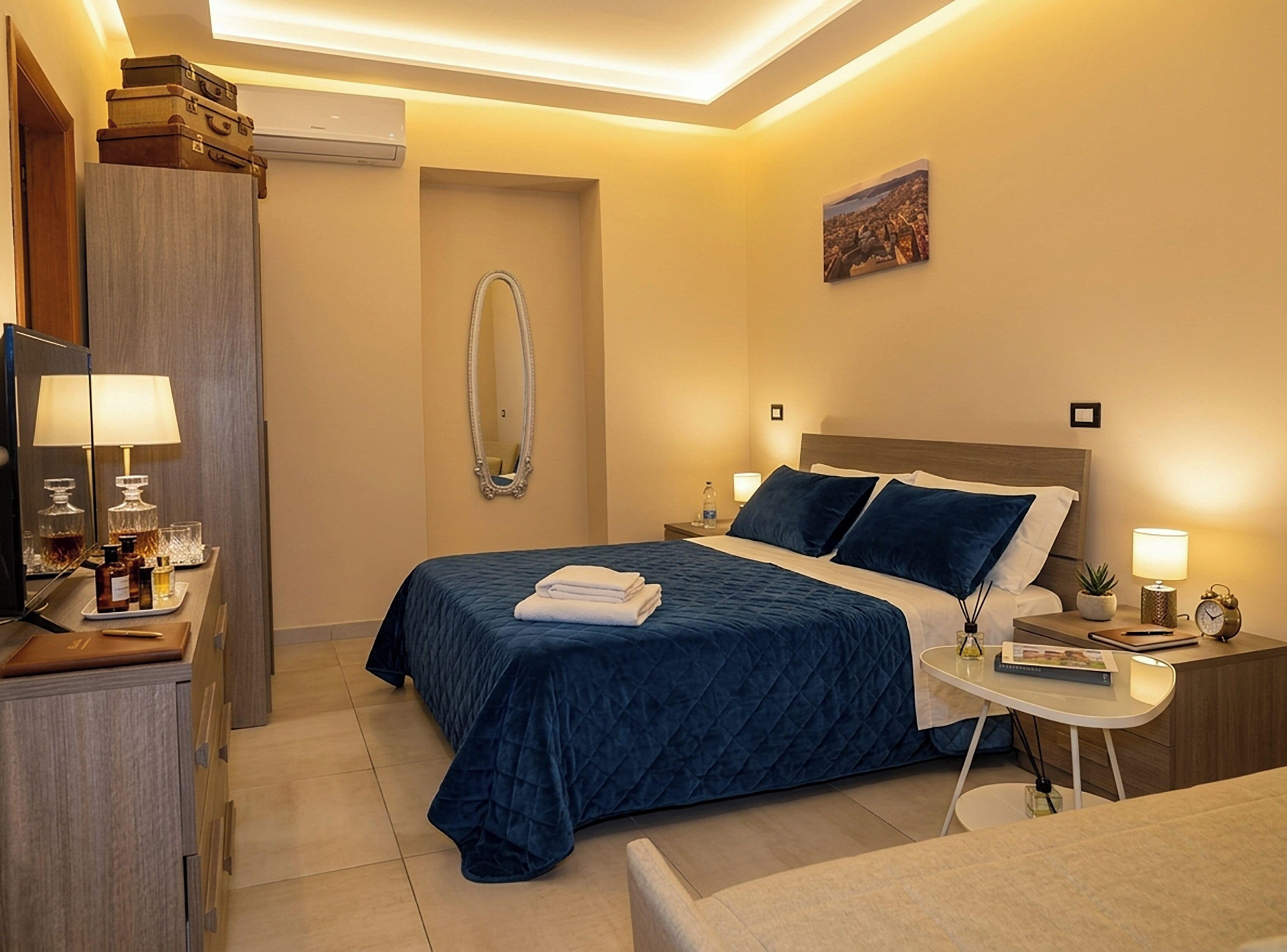 A hotel room with a bed, bedside tables, a desk with a lamp, a mirror, and a painting on the wall.