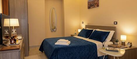 A hotel room with a bed, bedside tables, a desk with a lamp, a mirror, and a painting on the wall.