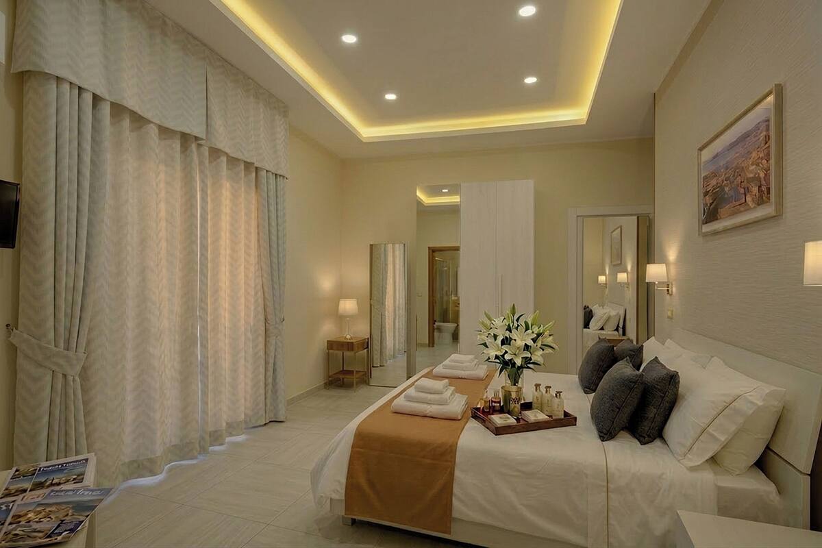 A hotel room with a large bed, a bedside table with a lamp, a mirror, and a view of the bathroom.