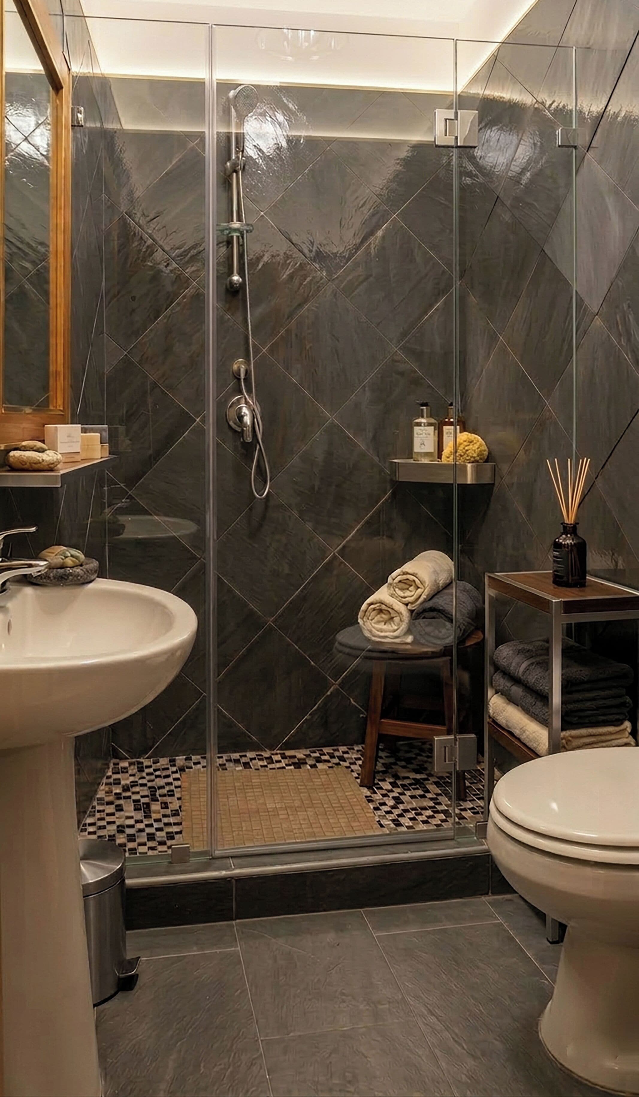 A modern bathroom with a glass-enclosed shower, a sink, a toilet, and a small stool with towels.