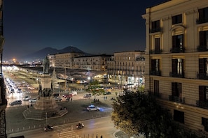 A nighttime cityscape with a prominent statue in a square, surrounded by buildings and a mountain in the background. - MaX RelaX Suite (Naples)