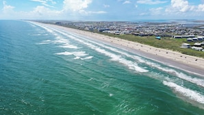 Vue aérienne d’une zone côtière avec une plage, des bâtiments et un ciel dégagé.