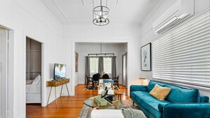 A modern living room with a teal sofa, a coffee table, and a TV. There is a dining area with chairs and a table in the background. - Wandal Haven • 3BR • King • + 2 Doubles • Pets OK (Rockhampton)