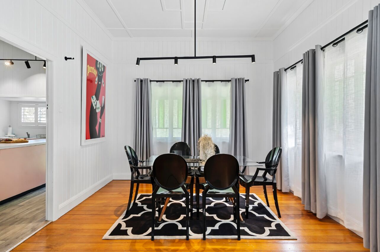 Un coin repas avec une table dressée pour quatre personnes, un tapis noir et blanc et des rideaux gris.