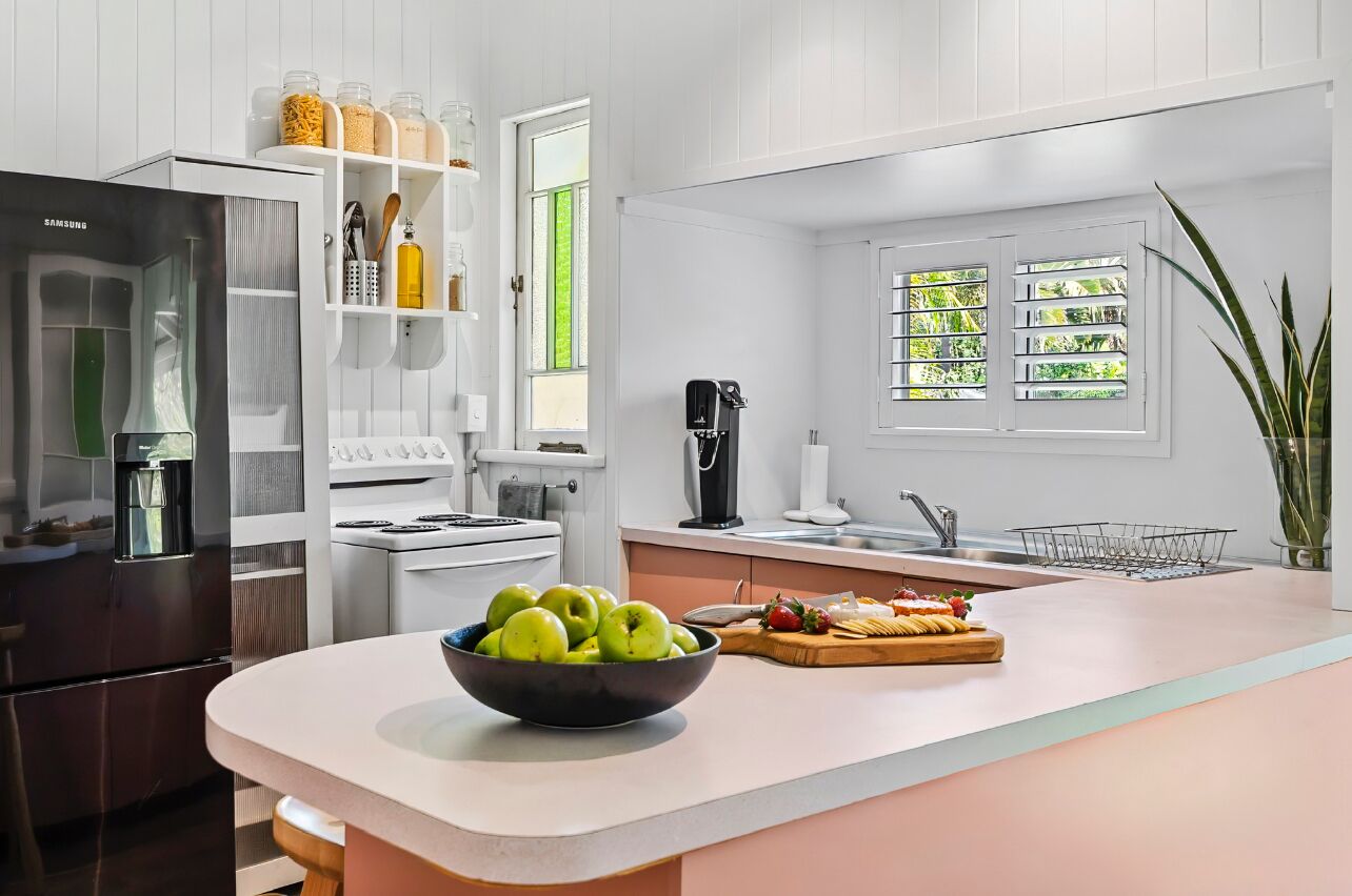 A modern kitchen with white cabinetry, a stainless steel refrigerator, a coffee maker, and a bowl of green apples on the counter.