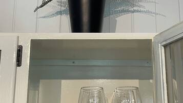 A cabinet with a potted fern on top and several wine glasses inside.