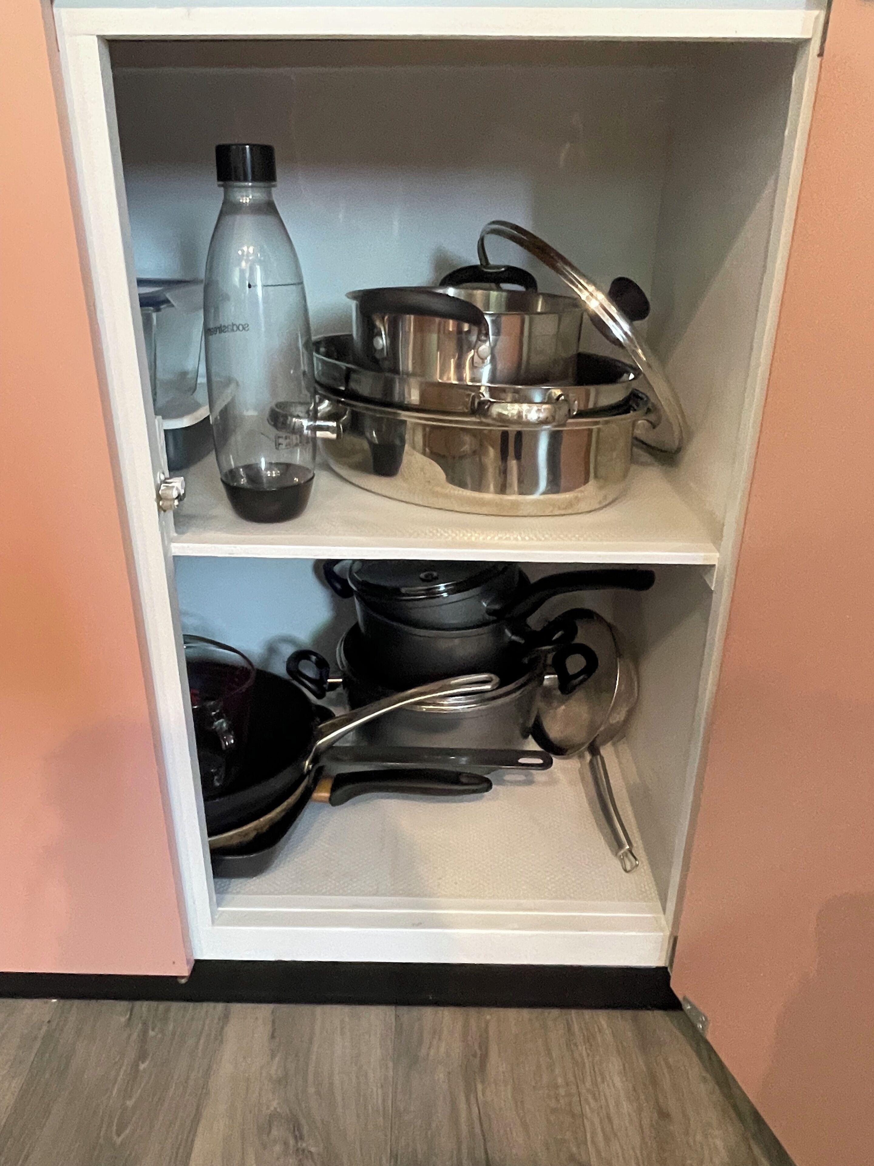 A kitchen cabinet with stainless steel cookware, including pots and pans, and a water bottle.
