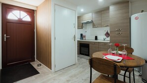 A compact kitchen with a wooden door, white cabinets, a built-in oven, and a dining area with a round table and chairs.