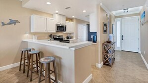 A kitchen with white cabinets, a central island with stools, a microwave, and a refrigerator. - Enjoy a serene harbor view in this spacious 2-bedroom condo in Placida. (Placida)