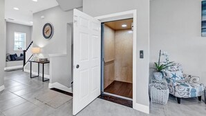 A modern interior with a hallway leading to an elevator, a staircase, and a seating area with a lamp. - Stay in comfort at Landings 126 in Placida: a spacious 3BR retreat! (Placida)
