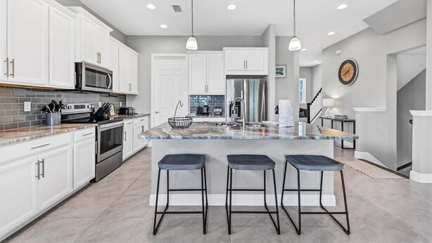 A modern kitchen with white cabinets, a large island with bar stools, stainless steel appliances, and pendant lighting. - Stay in comfort at Landings 126 in Placida: a spacious 3BR retreat! (Placida)