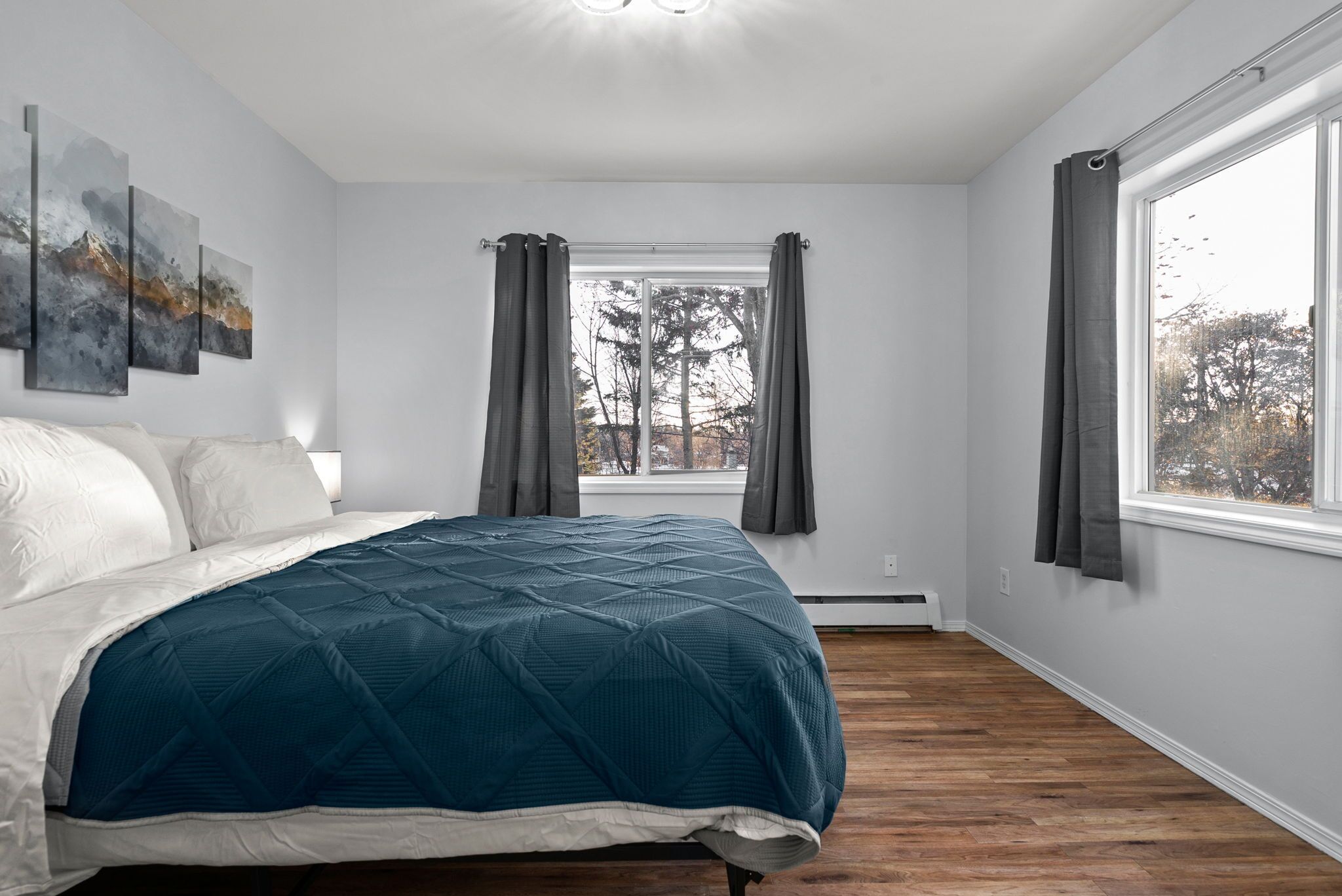 A bedroom with a bed, a window with curtains, and a wall-mounted artwork.