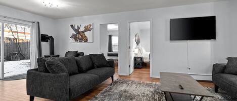 Een moderne woonkamer met een grijze bank, een salontafel en een flatscreen-tv aan de muur.