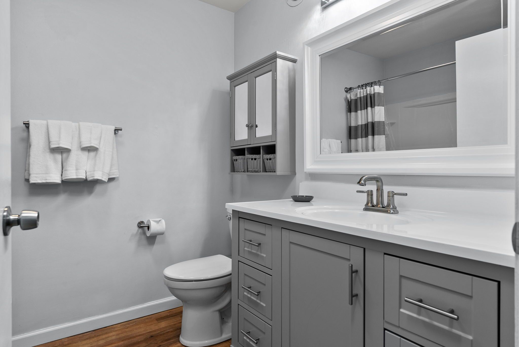 A modern bathroom with a toilet, a sink with a mirror, and a cabinet with baskets.