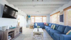 Ein Wohnzimmer mit blauem Sofa, einem Couchtisch, einem an der Wand montierten Fernseher und einem Bücherregal.