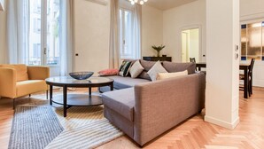 Ein modernes Wohnzimmer mit Sofa, Sessel und Couchtisch. Es gibt einen Essbereich mit Tisch und Stühlen.