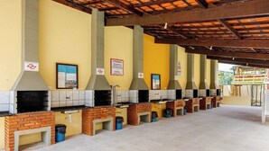 Una hilera de estaciones de cocina al aire libre con mostradores de ladrillo y paredes con azulejos, bajo un área techada con piso de baldosas.