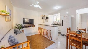 Una cocina moderna con una isla central, un comedor con sillas de madera, un sofá con cojines y un ventilador de techo.