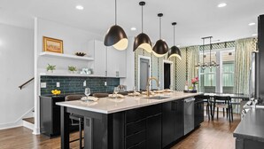 A modern kitchen with a large island, black cabinetry, and pendant lighting. - 2 Homes | 24 Guests | Rooftop Hot Tub Fire Pit (Nashville)