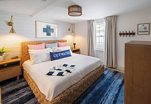 Ein ordentlich eingerichtetes Schlafzimmer mit einem großen Bett, einem Nachttisch, einer Lampe, einem Blumentopf und einem Fenster mit Vorhängen.