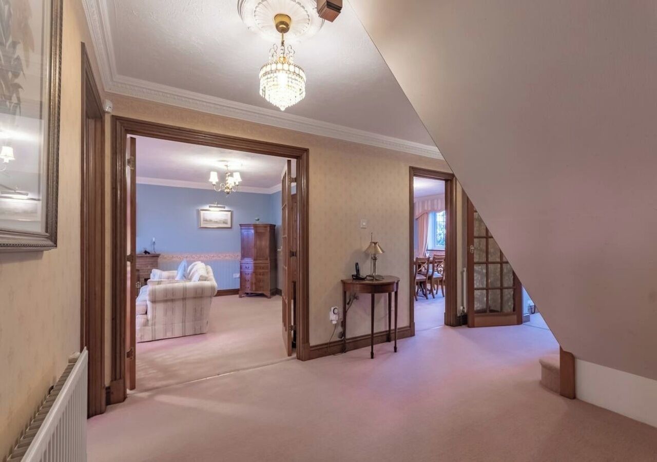 Un hallo espacioso con candelabro, escalera y zona de comedor con mesa y sillas.