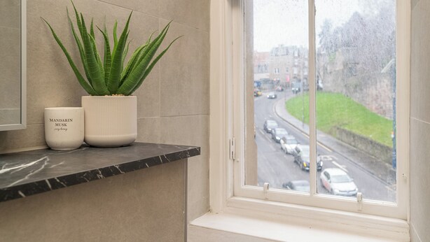 A bathroom with a marble countertop, a potted aloe vera plant, and a window overlooking a street with cars. - Charming 2-Bed flat Steps from the Royal Mile - Pass the Keys (Edinburgh)