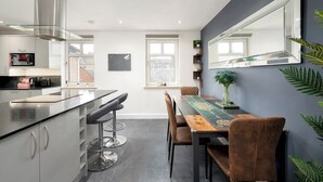 A modern kitchen with a central island, bar stools, and a dining table with chairs. There is a large mirror on the wall and a window providing natural light. - Stylish 2-Bed Flat with Balcony Near Haymarket - Pass the Keys (Edinburgh)