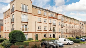 A multi-story residential building with a brick facade, multiple balconies, and a parking area with cars. - Stylish 2-Bed Flat with Balcony Near Haymarket - Pass the Keys (Edinburgh)