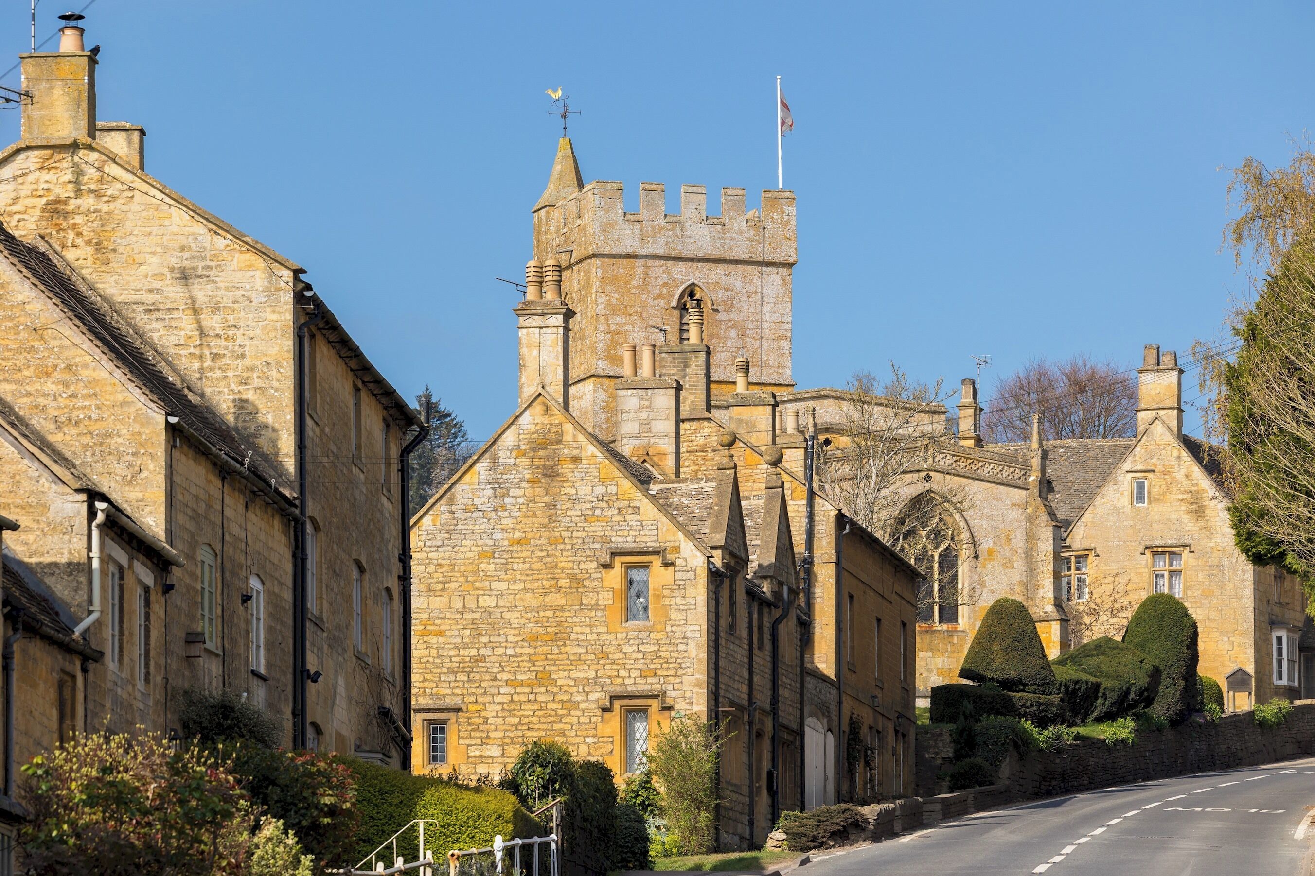 A historic stone building with a prominent tower, featuring a traditional architectural style with arched windows and a flag on top.