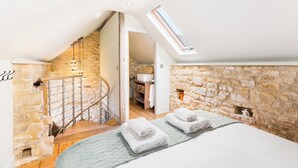 Ein Schlafzimmer mit Steinswand, Oberlicht, Treppe und einem Bett mit Handtüchern.