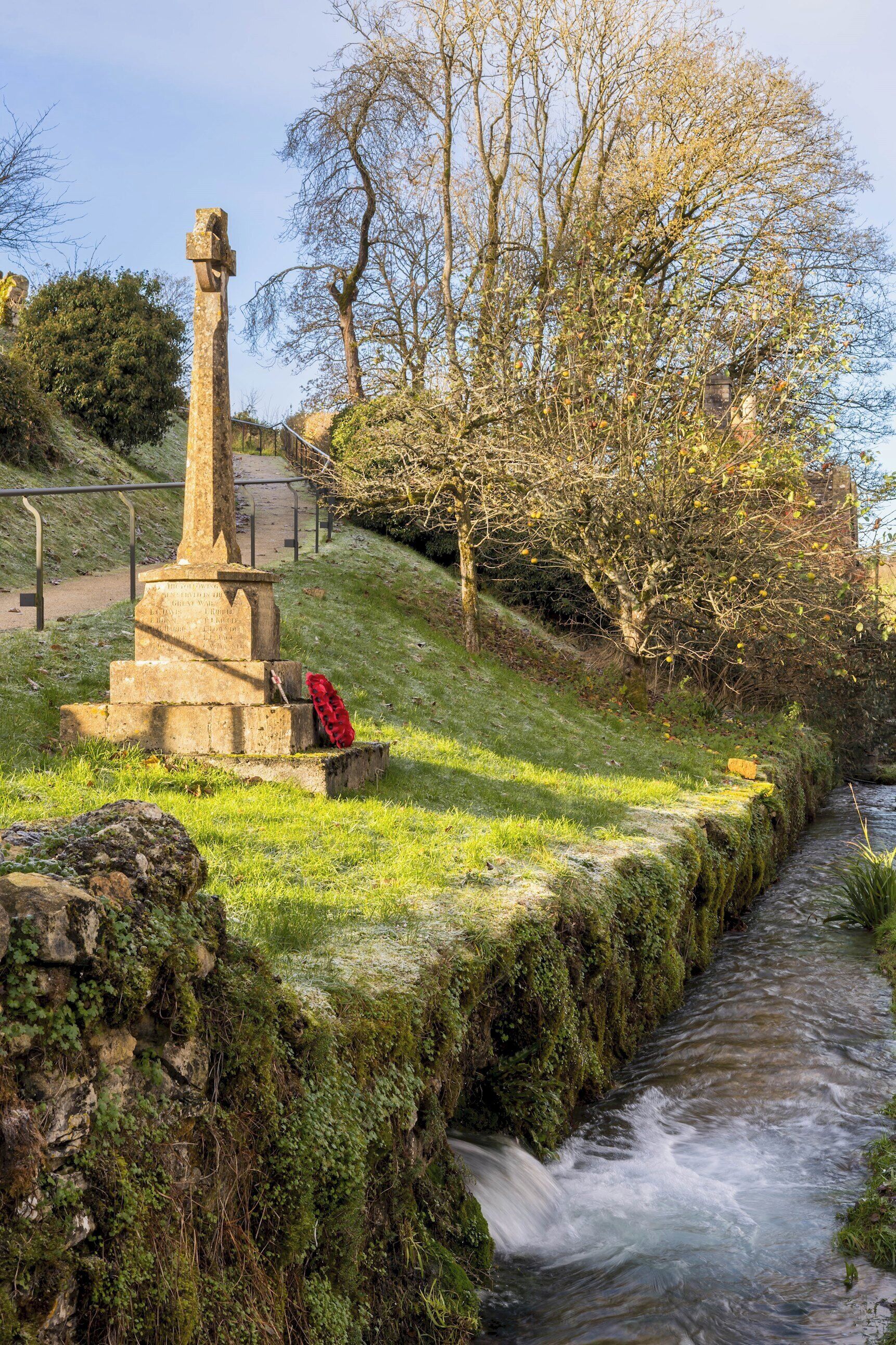 A stone monument with a cross, a red poppy, and a flowing stream.