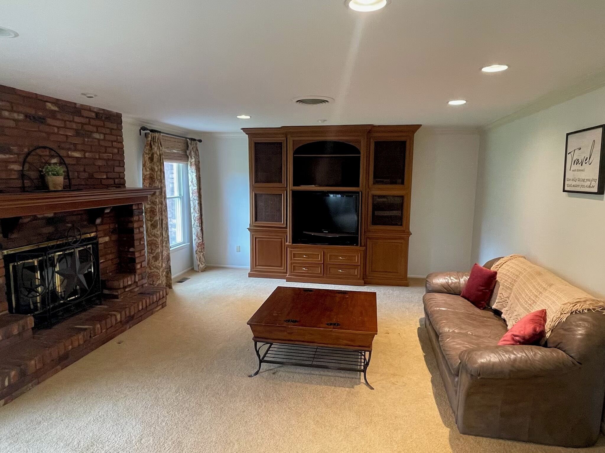 A living room with a brick fireplace, a wooden entertainment center, a leather sofa, and a coffee table.