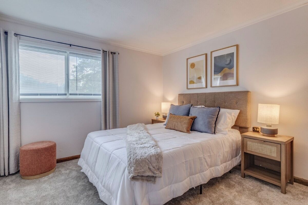 A bedroom with a large bed, bedside tables, a nightstand, a window with curtains, and two framed pictures on the wall.